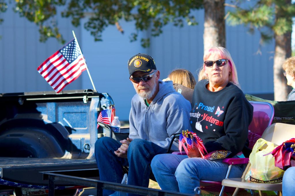 pexels photo 34148638 Senior veteran couple in a parade setting with American flags, showcasing patriotism and community spirit.