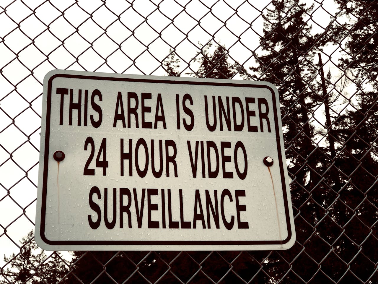 gallery-4 Sign on a chain-link fence stating 'This area is under 24 hour video surveillance.'