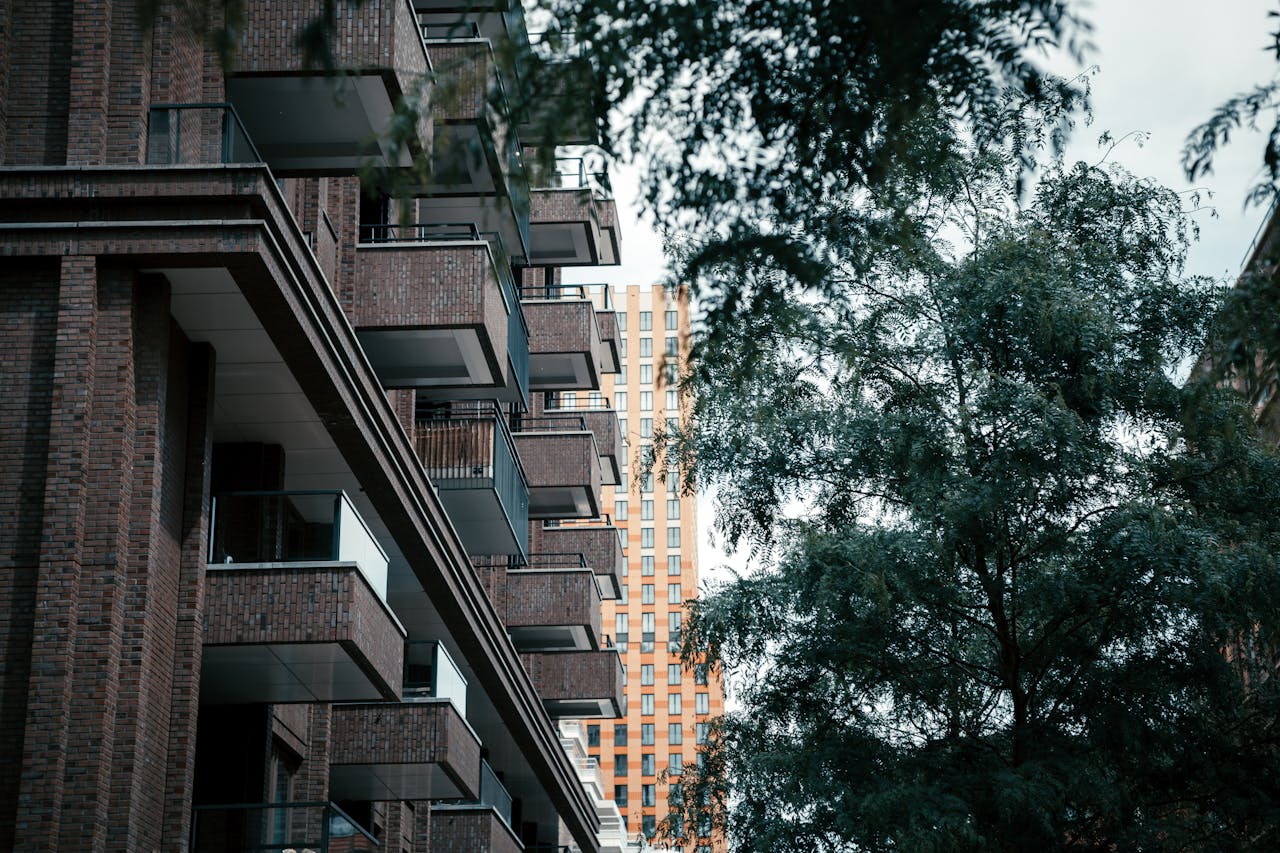 hero-img-01 Low-angle view of brick residential buildings with lush greenery.